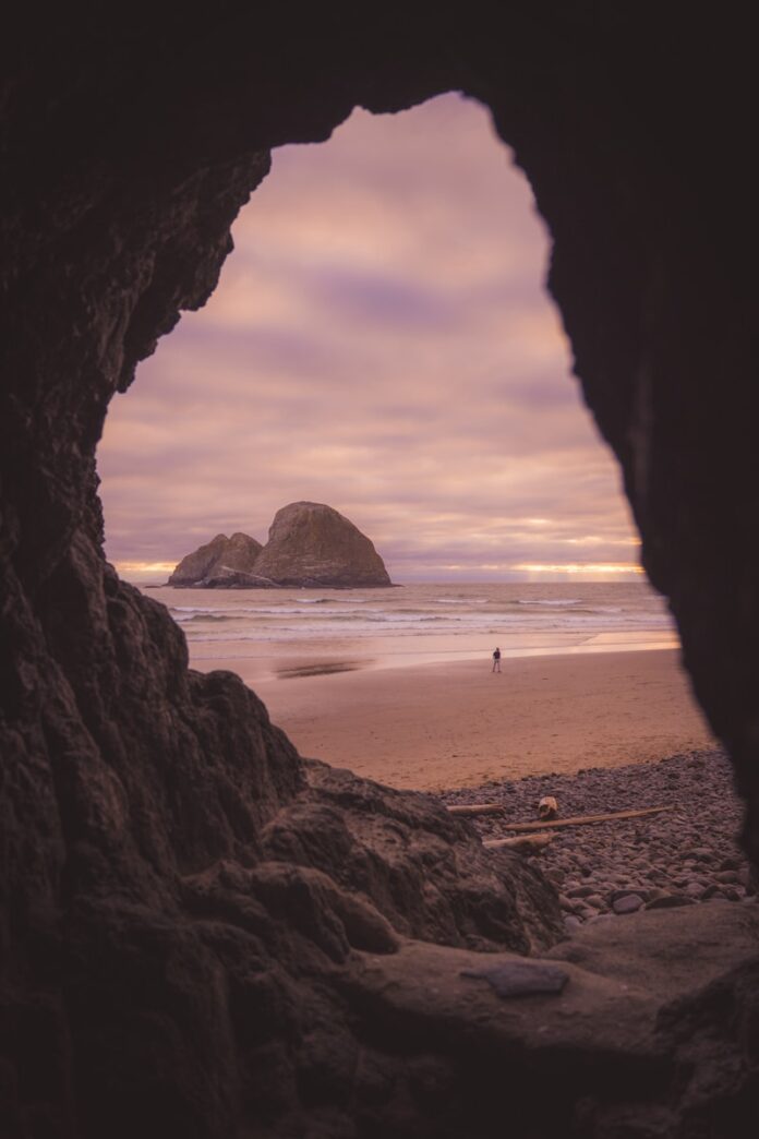 Sea stack and beach visible through a dark cave opening.